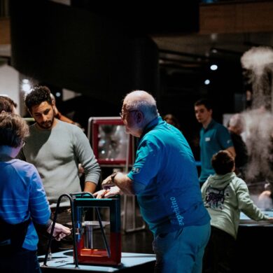 Mehrere Personen stehen in einem nächtlichen Museum um angestrahlte Technik-Exponate herum