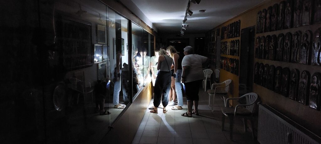 Mehrere Personen werden im Dunkeln durch den Gang eines kleinen Museums geführt und betrachten eine Vitrine linkerhand