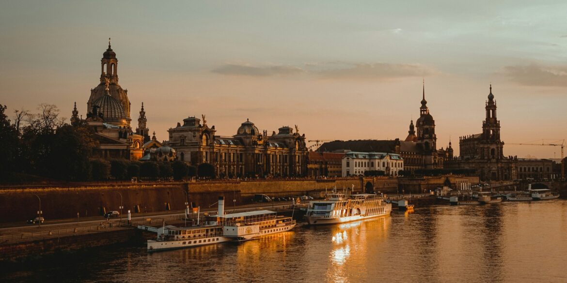 Die Dächer der Dresdner Altstadt, mit Landtag und Frauenkirche, liegen am Elbufer im roten Licht der Abendsonne.