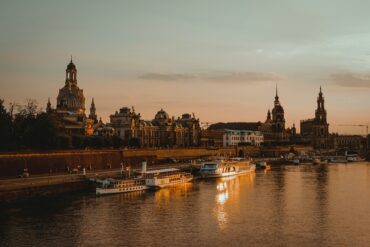 Die Dächer der Dresdner Altstadt, mit Landtag und Frauenkirche, liegen am Elbufer im roten Licht der Abendsonne.