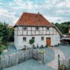 Das Ferienhaus Gänsetrappe im Harz von aussen; ein zweigeschossiges Fachwerkhaus mit rotem Ziegeldach, davor ein mit Kies bedeckter Hof