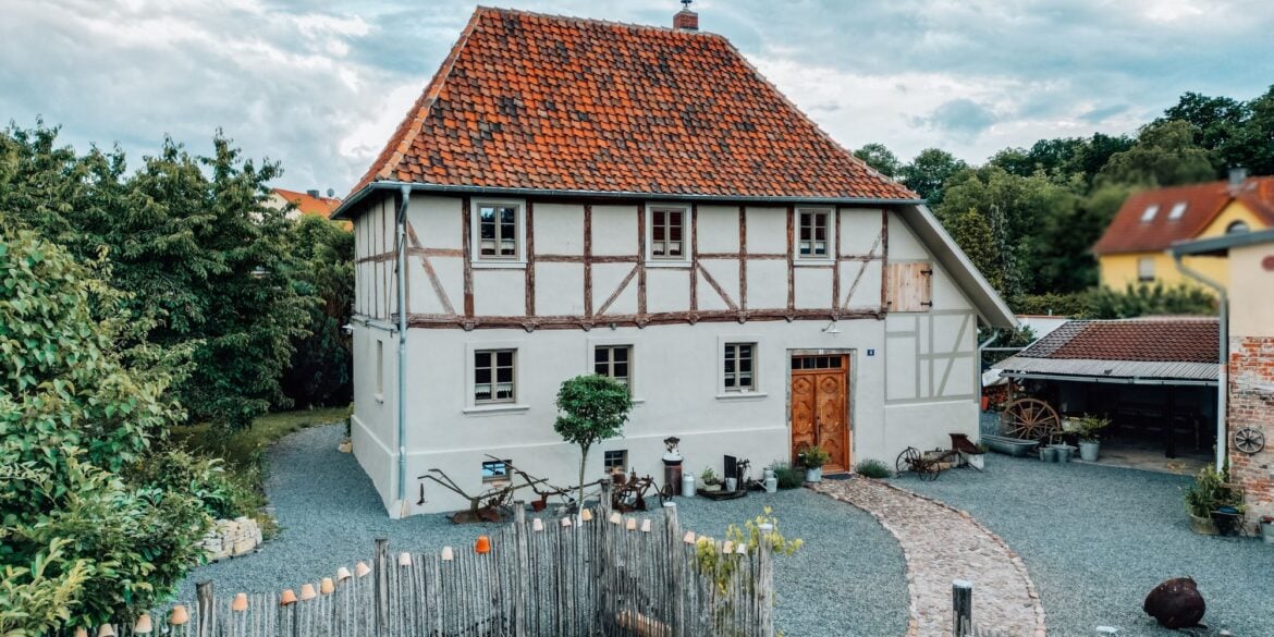 Das Ferienhaus Gänsetrappe im Harz von aussen; ein zweigeschossiges Fachwerkhaus mit rotem Ziegeldach, davor ein mit Kies bedeckter Hof