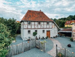 Das Ferienhaus Gänsetrappe im Harz von aussen; ein zweigeschossiges Fachwerkhaus mit rotem Ziegeldach, davor ein mit Kies bedeckter Hof