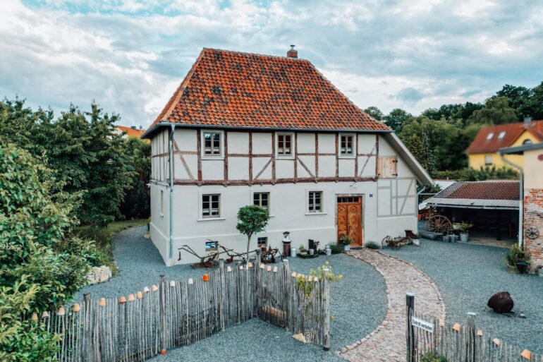 Das Ferienhaus Gänsetrappe im Harz von aussen; ein zweigeschossiges Fachwerkhaus mit rotem Ziegeldach, davor ein mit Kies bedeckter Hof