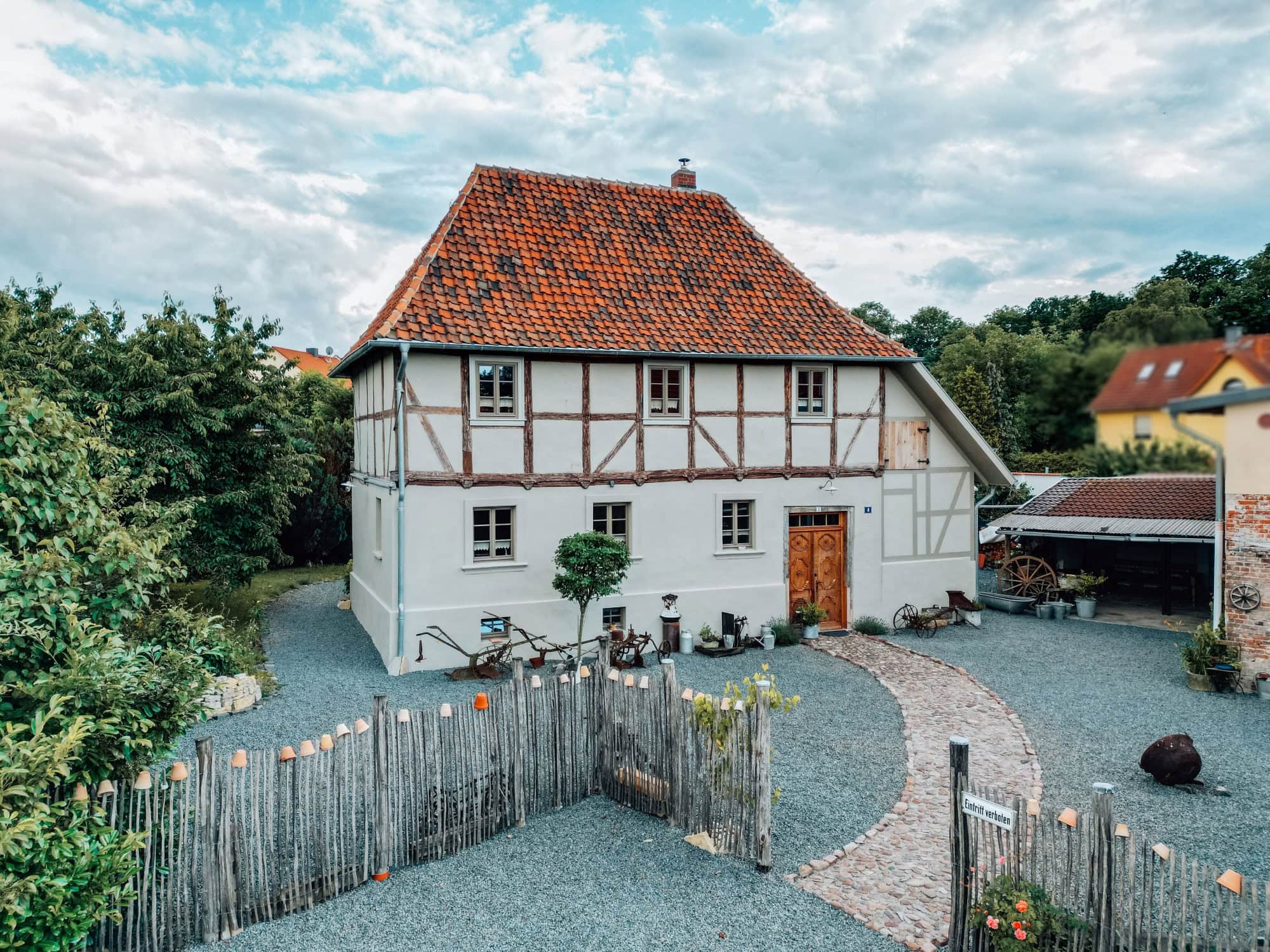 Das Ferienhaus Gänsetrappe im Harz von aussen; ein zweigeschossiges Fachwerkhaus mit rotem Ziegeldach, davor ein mit Kies bedeckter Hof