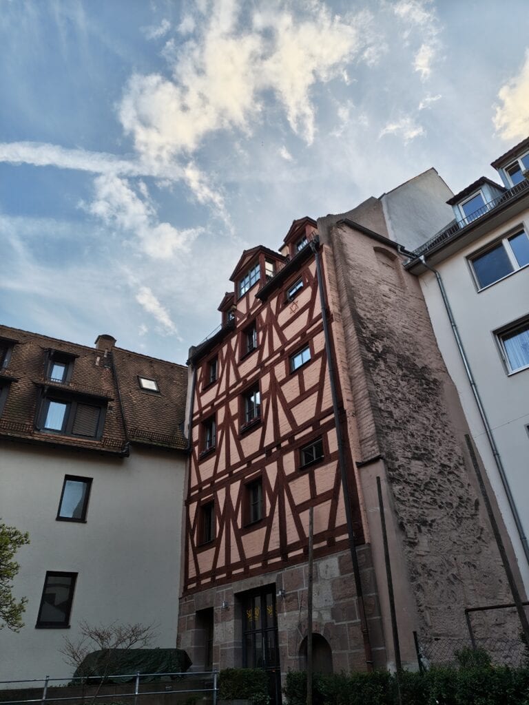 Ein Fachwerkhaus mit rosa Putz ragt in die Höhe. Rechts und links daneben zwei weiß verputzte Häuser
