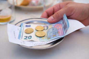 A metal tablet with a 20-Euro-bill atop of a receipt and some cents on it, grabbed by a hand