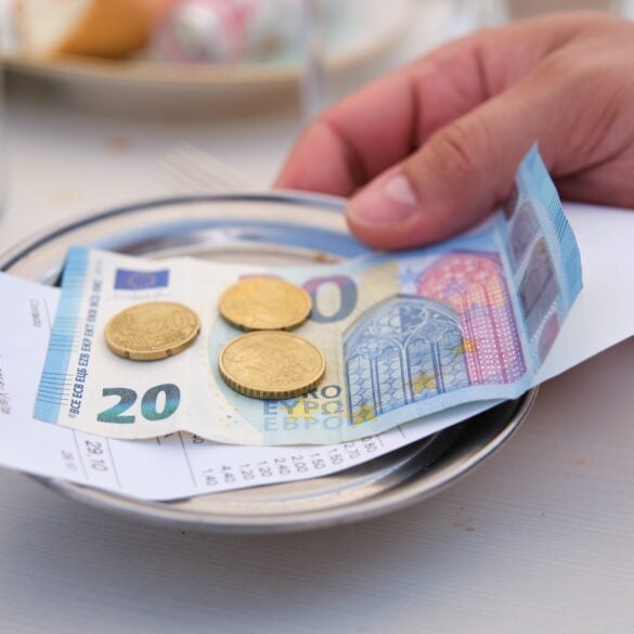 A metal tablet with a 20-Euro-bill atop of a receipt and some cents on it, grabbed by a hand