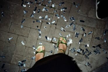 Ein Paar Füße in grün-glänzenden High-Heels stehen auf Pflastersteinen, rundherum silbernes Konfetti. Das Foto sieht aus, wie von der Fußinhaberin selbst fotografiert.