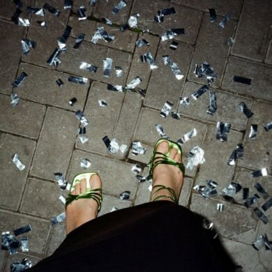 Ein Paar Füße in grün-glänzenden High-Heels stehen auf Pflastersteinen, rundherum silbernes Konfetti. Das Foto sieht aus, wie von der Fußinhaberin selbst fotografiert.