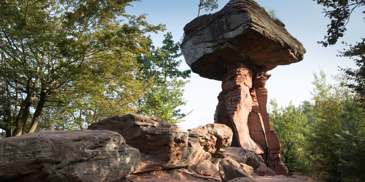 Auf einer roten Sandsteinsäule ruht ein riesiger Sandsteinquader; ein wenig sieht die Formation aus wie ein Tisch. Rundum weitere Sandsteinfelsen, der Himmel darüber blau
