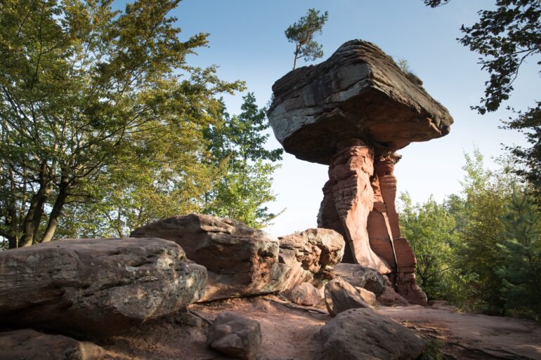 Auf einer roten Sandsteinsäule ruht ein riesiger Sandsteinquader; ein wenig sieht die Formation aus wie ein Tisch. Rundum weitere Sandsteinfelsen, der Himmel darüber blau