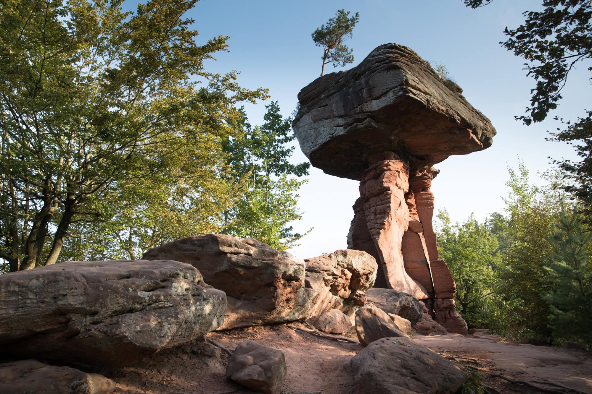 Auf einer roten Sandsteinsäule ruht ein riesiger Sandsteinquader; ein wenig sieht die Formation aus wie ein Tisch. Rundum weitere Sandsteinfelsen, der Himmel darüber blau