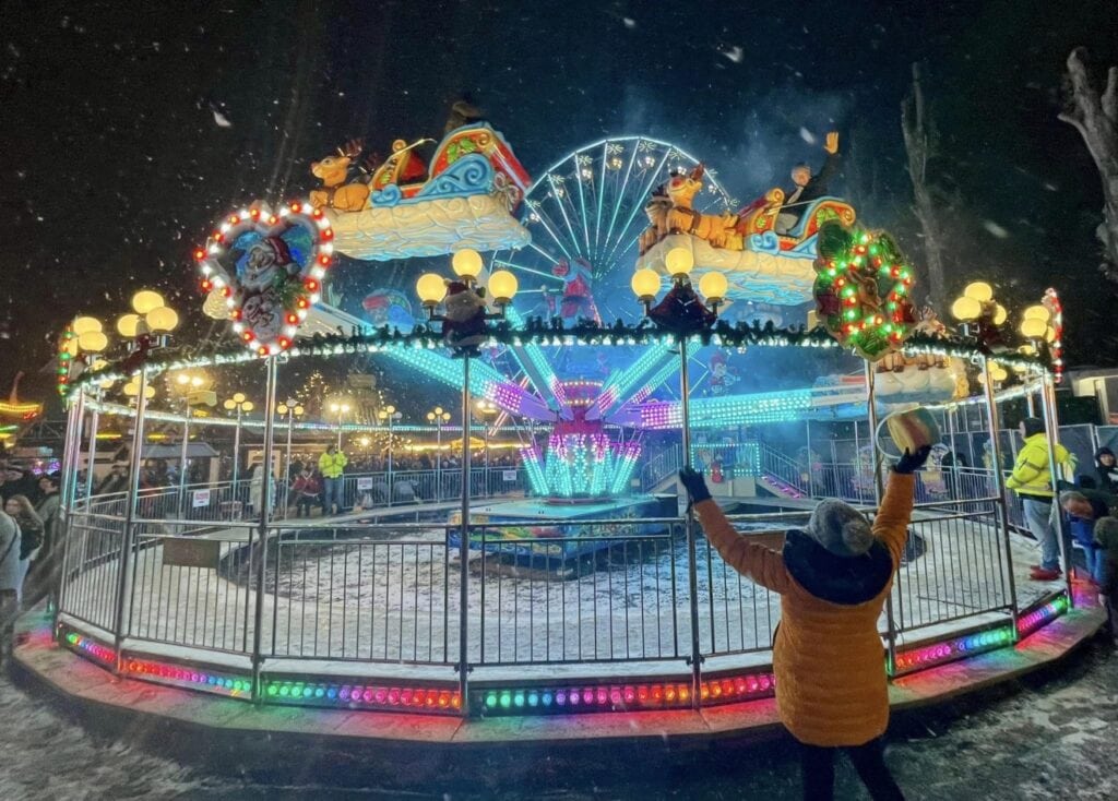 A child cheering on a brightly and colorfully illuminated carousel at a christmas market.
