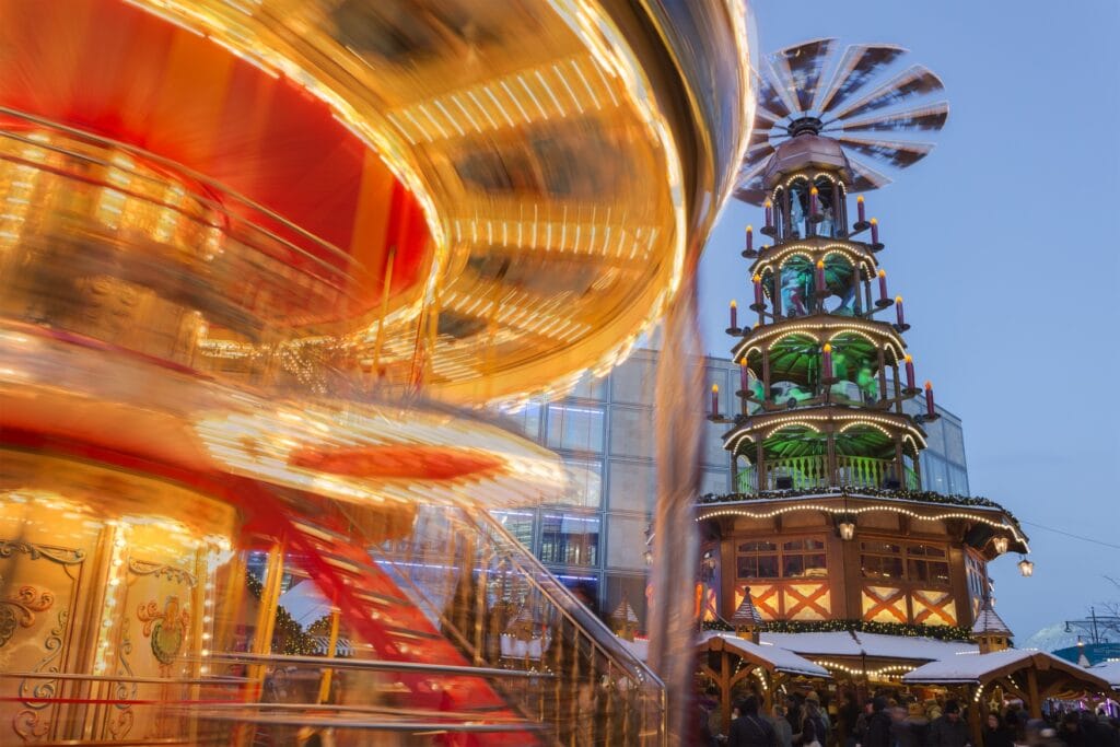 A fast moving carousel at a christmas market. In the background there is a giant christmas pyramid.