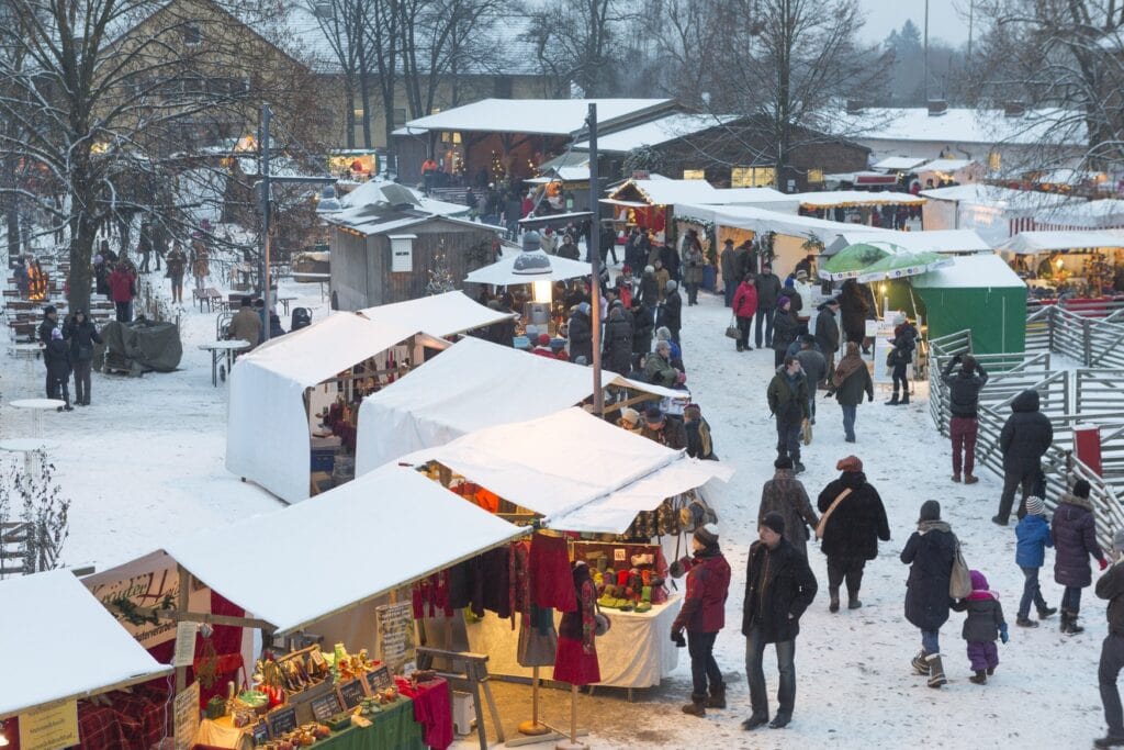 Multiple rows of huts on a christmas market. Many people are visiting, everything is covered in snow.