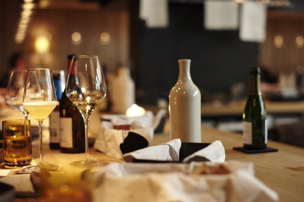 Auf einem Restauranttisch stehen mehrere Getränke, einige Brotkörbe und eine tönerne Flasche Olivenöl, alles in einer warmen Lichtstimmung.