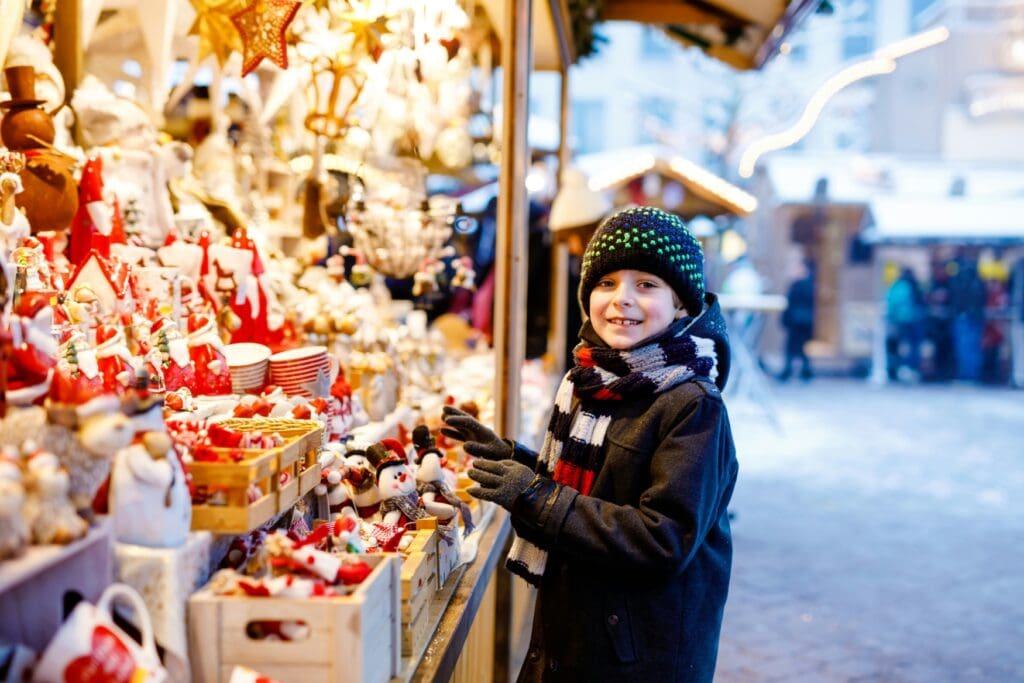 A child at a christmas market hut thats selling decorative articles. The child smiles directly into the camera.