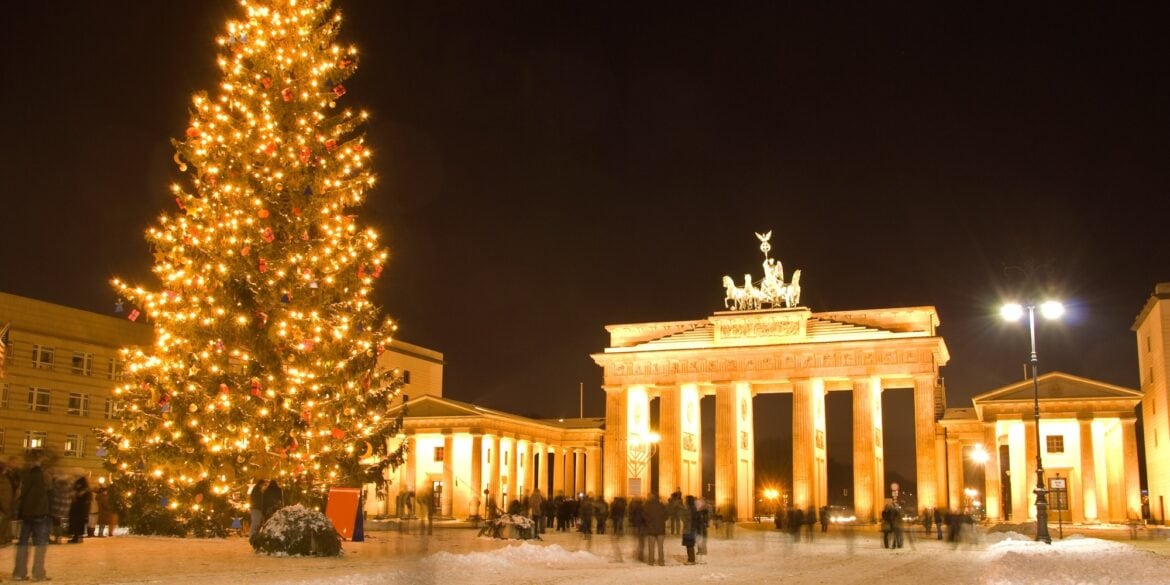 The Brandenburg Gate in Berlin at night, brightly illuminated and with a giant christmas tree in front of it.