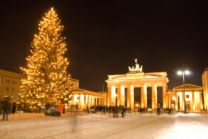The Brandenburg Gate in Berlin at night, brightly illuminated and with a giant christmas tree in front of it.