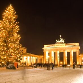 The Brandenburg Gate in Berlin at night, brightly illuminated and with a giant christmas tree in front of it.