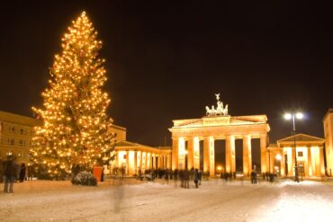 The Brandenburg Gate in Berlin at night, brightly illuminated and with a giant christmas tree in front of it.