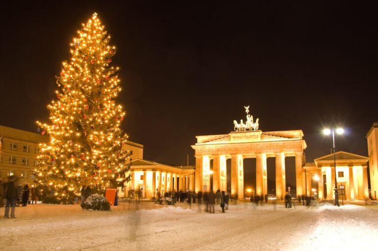 The Brandenburg Gate in Berlin at night, brightly illuminated and with a giant christmas tree in front of it.