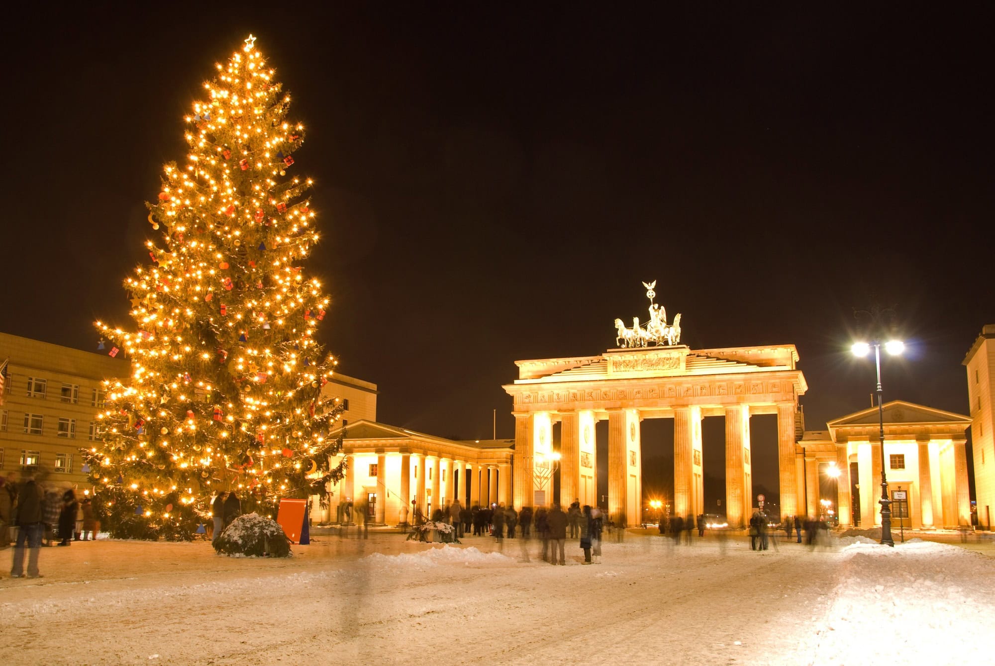 The Brandenburg Gate in Berlin at night, brightly illuminated and with a giant christmas tree in front of it.