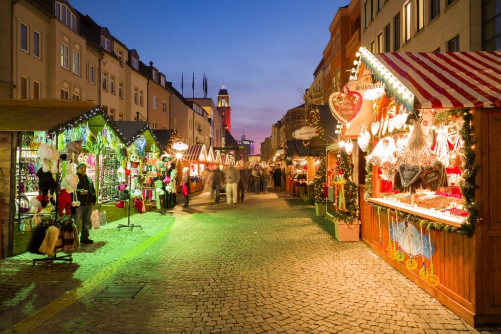 Long exposure of visitors walking along a road on a brightly illuminated christmas markets, with huts to both sides.