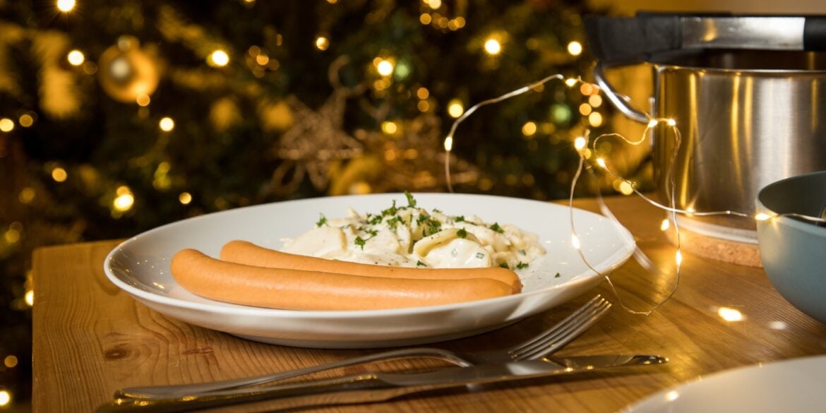 Eine Portion Kartoffelsalat mit zwei Bockwürsten, angerichtet auf einem weihnachtlich dekorierten Tisch