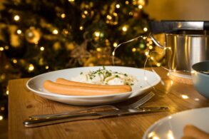 Eine Portion Kartoffelsalat mit zwei Bockwürsten, angerichtet auf einem weihnachtlich dekorierten Tisch