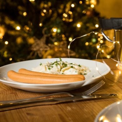 Eine Portion Kartoffelsalat mit zwei Bockwürsten, angerichtet auf einem weihnachtlich dekorierten Tisch
