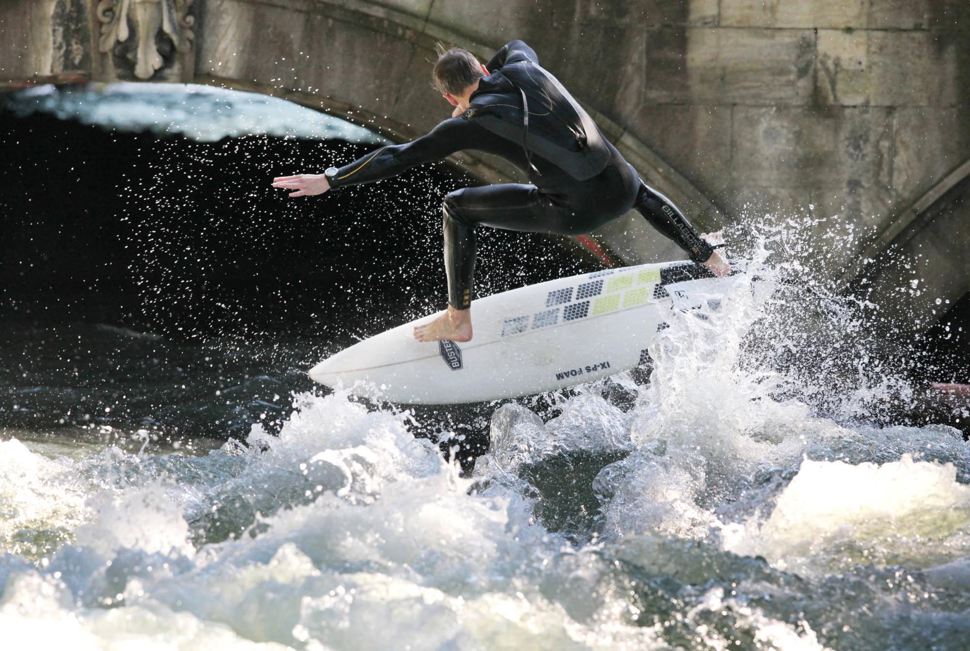 A man in a wetsuit is pushed up by a wave on his surfboard. He has his arms outstretched on both sides.