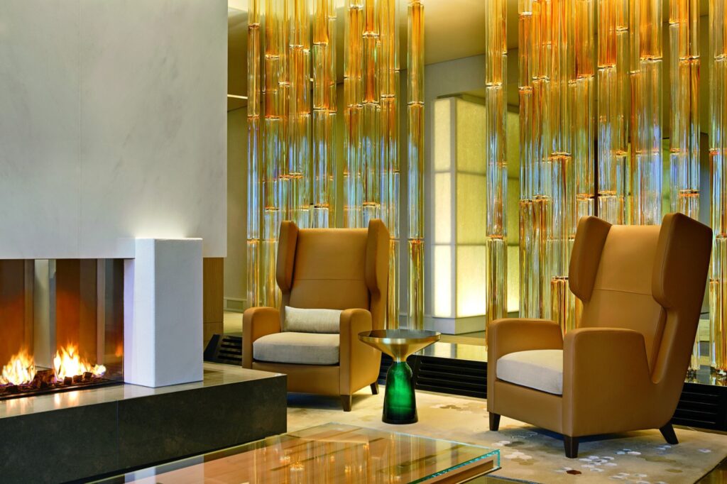 Two wing chairs stand in a modern setting in front of a lit fireplace.