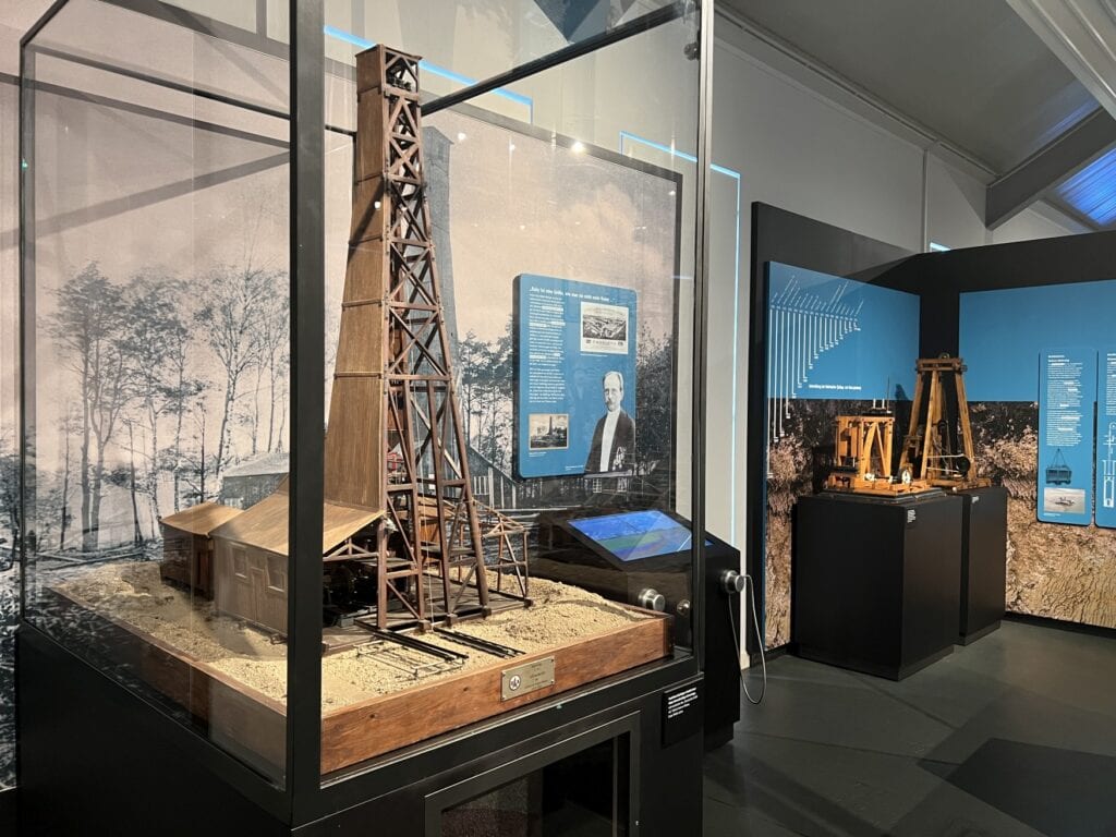 Modell eines hölzernen Erdölturms in einer Vitrine in einem Musem. Rechts daneben ein weiteres Modell.