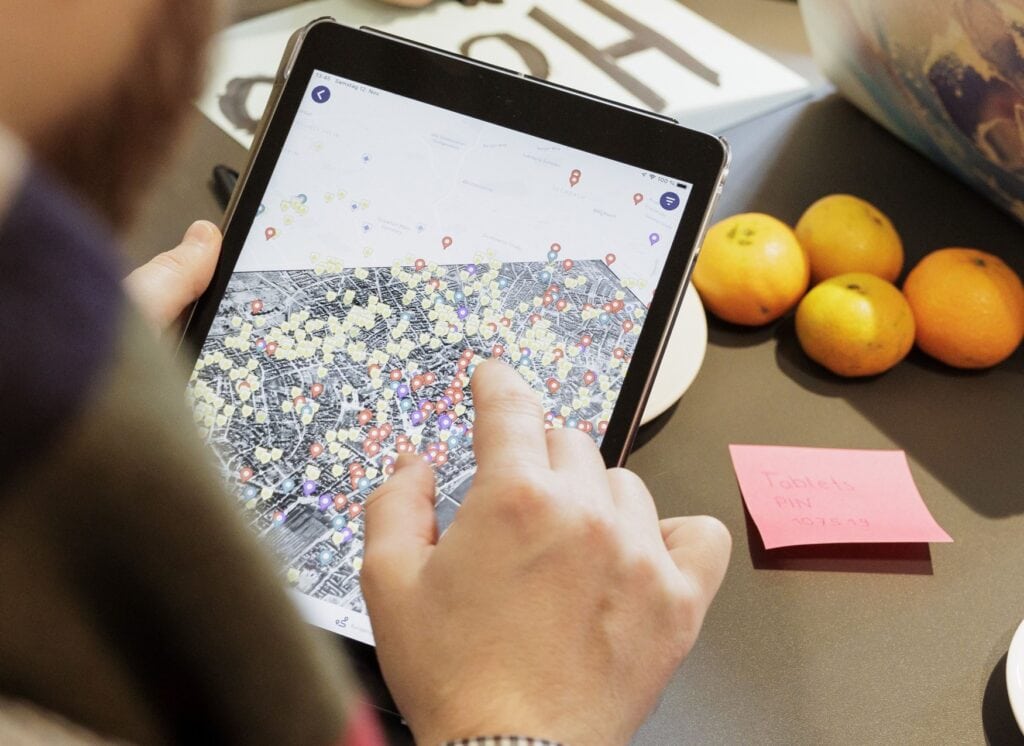 Eine Person manövriert auf einem Pad durch eine Karten-App über eine digitale Karte von Frankfurt, auf der zahlreiche Orte eingezeichnet sind.