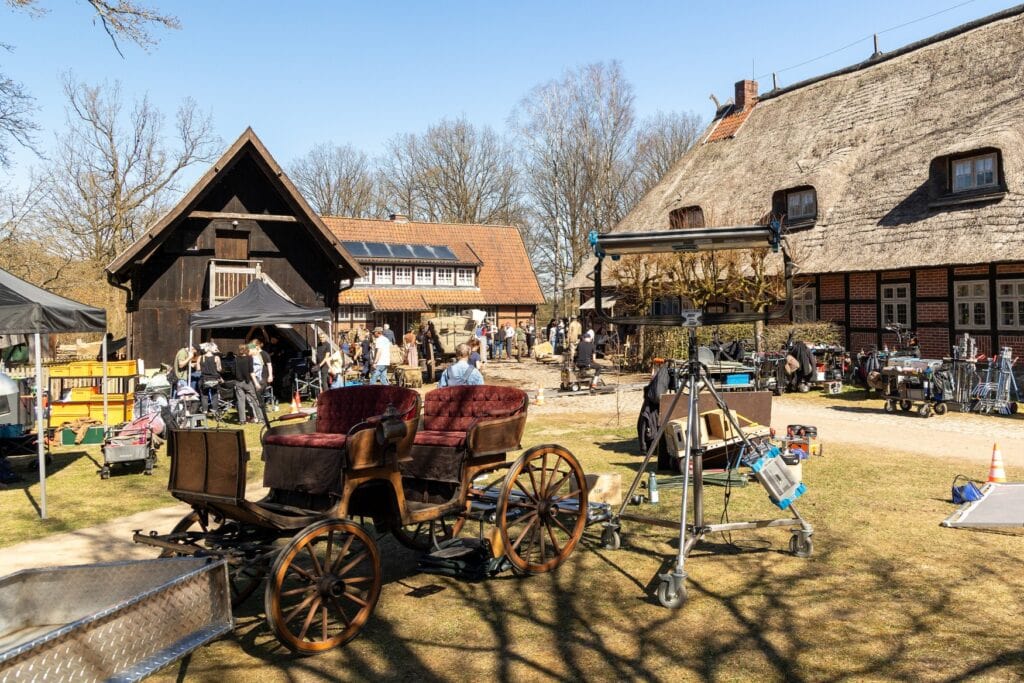 Im Innenhof eines historischen Landguts mit Ziegelfassade und Reetdächern sind viele Menschen unterwegs, dazwischen Technik, die für einen Filmdreh benötigt wird.