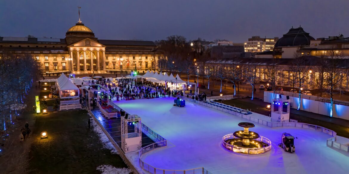 Vor dem klassizistischen Staatstheater Wiesbaden, hell erleuchtet, liegt eine lange Eisbahn, auf der viele Menschen fahren.