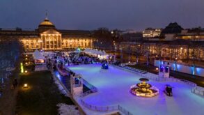 Vor dem klassizistischen Staatstheater Wiesbaden, hell erleuchtet, liegt eine lange Eisbahn, auf der viele Menschen fahren.