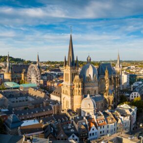 Stadtbild von Aachen mit dem Dom im Zentrum. Am prominentesten eine achteckige Kuppel in der Mitte, rechts daneben der Kirchenchor mit hohen gotischen Fenster.