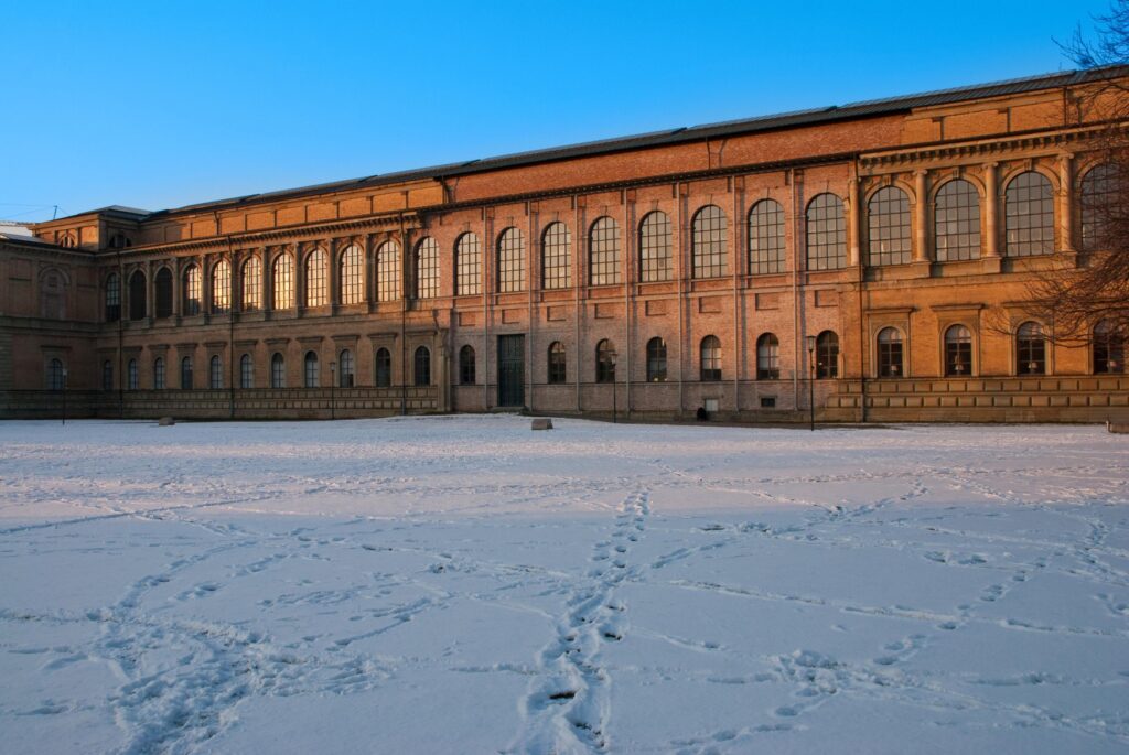 The Alte Pinakothek in the winter sun. Several footprints stretch across the snow-covered lawn in front of it.