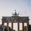 Das Brandenburger Tor im Sommer, davor zieht eine Reihe Seifenblasen von links nach rechts durchs Bild.