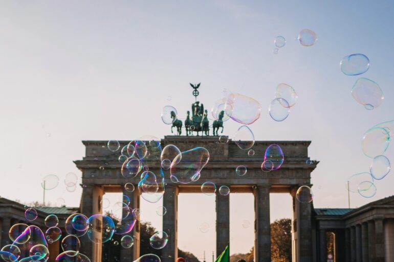 Das Brandenburger Tor im Sommer, davor zieht eine Reihe Seifenblasen von links nach rechts durchs Bild.