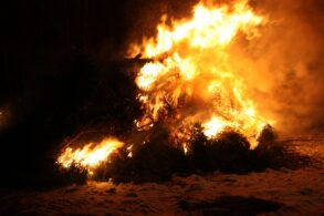 Auf einem nächtlichen Strand brennt ein großes Feuer in der Dunkelheit.