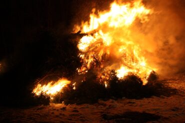 Auf einem nächtlichen Strand brennt ein großes Feuer in der Dunkelheit.