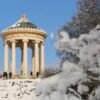 The circular Monopteros stands on a snow-covered hill. Many people are walking in the park in front of it.