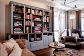 Die Bibliothek im Hotel "Zweite Heimat" in St. Peter-Ording; im Vordergrund eine Ledercouch mit hölzernem Couchtisch und Ledersessel gegenüber, an der Wand dahinter ein graues, vollgepacktes Holzregal. Rechts im Bild an der Ecke je ein bodentiefes Fenster.