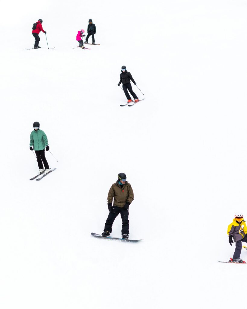 Close-up of several winter sports enthusiasts skiing and snowboarding down a snow-covered slope one after the other.
