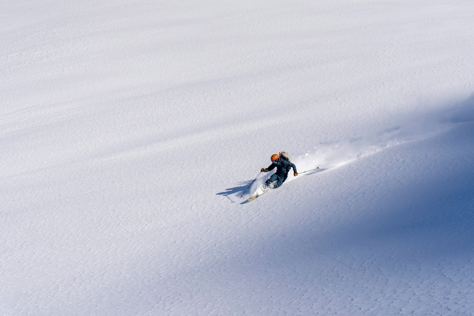 Drone footage of a skier speeding downhill through fresh, deep snow, leaving clouds of snow behind him.
