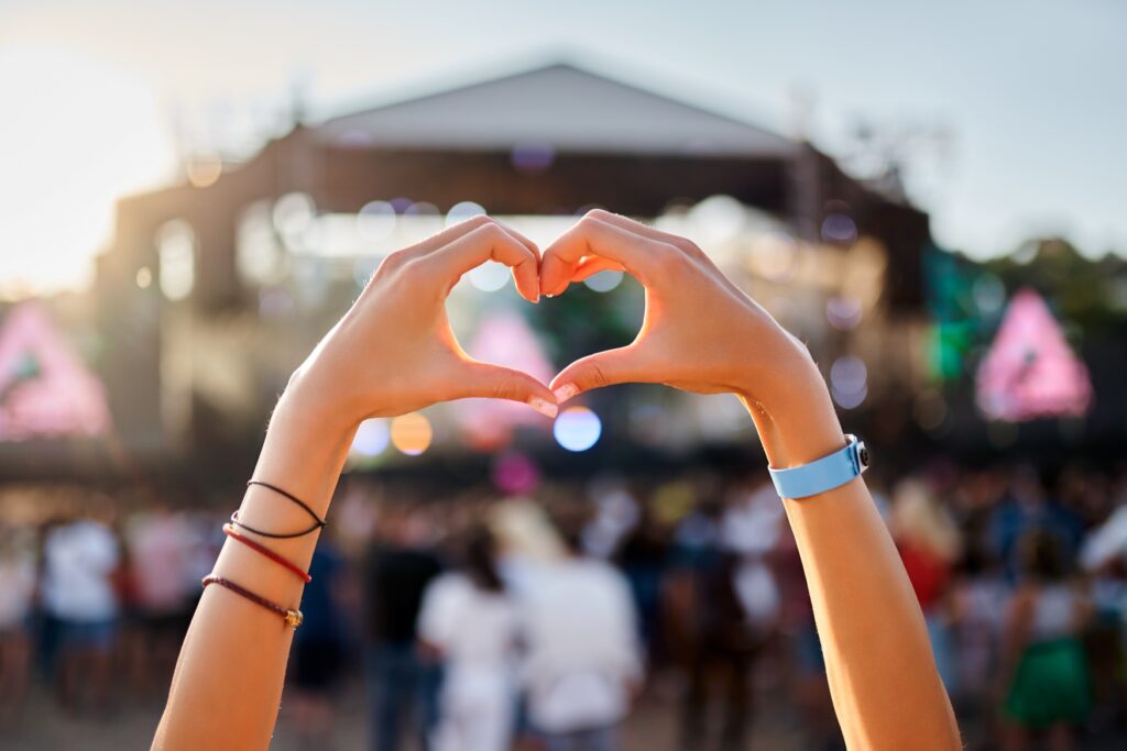 A person forms a heart with their hands at a festival